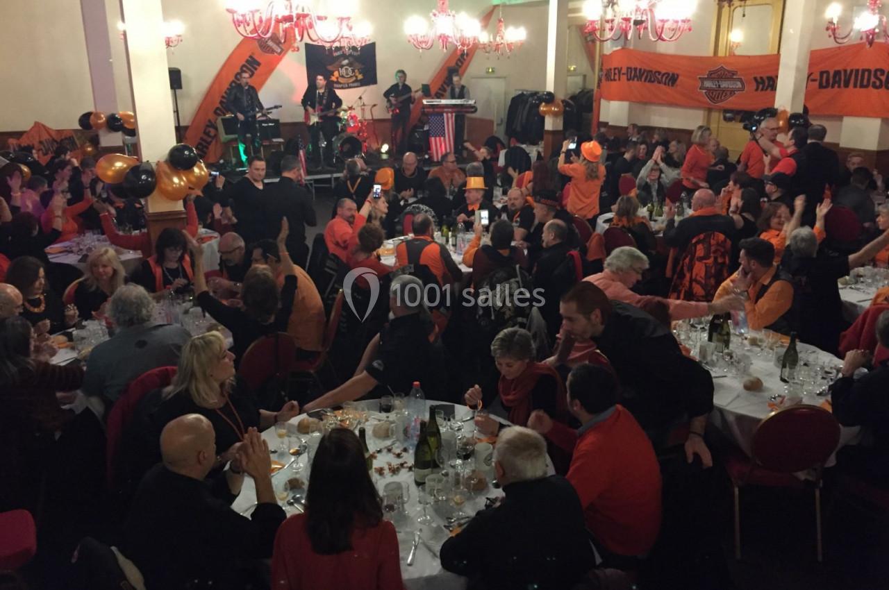 Salle remplie de convives attablés lors d'un événement festif avec un groupe de musique jouant sur scène.