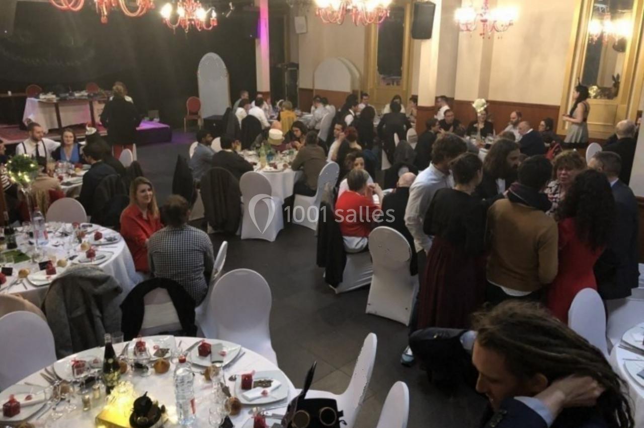 Des convives assis à des tables rondes décorées, participant à un dîner dans une salle éclairée par des lustres.