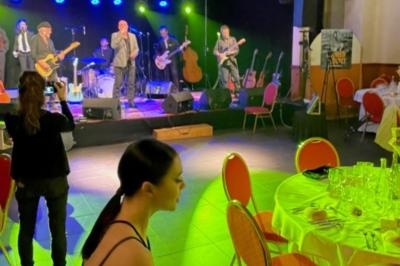 Salle sombre avec un public debout face à une scène éclairée où des musiciens jouent sous des projecteurs colorés.