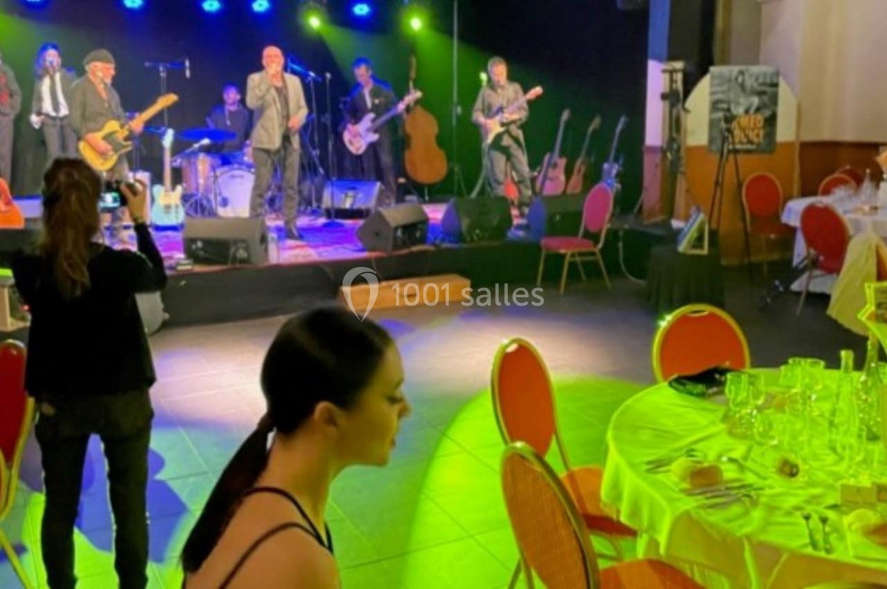 Groupe de musiciens jouant sur scène dans une salle éclairée, avec des tables dressées au premier plan.