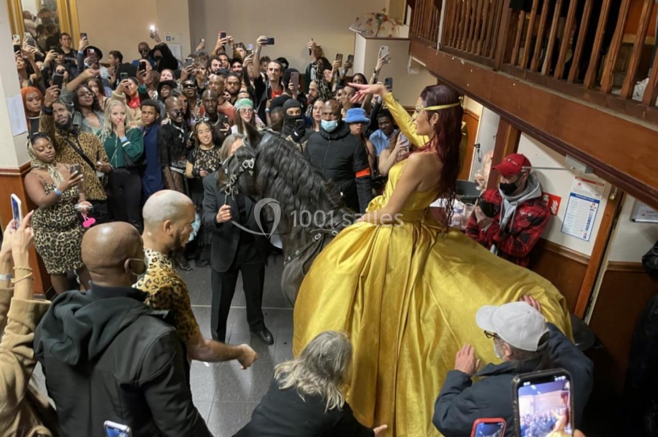 Une femme en robe dorée est assise sur un cheval noir dans une salle bondée de spectateurs.