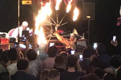 Salle sombre avec un public debout face à une scène éclairée où des musiciens jouent sous des projecteurs colorés.