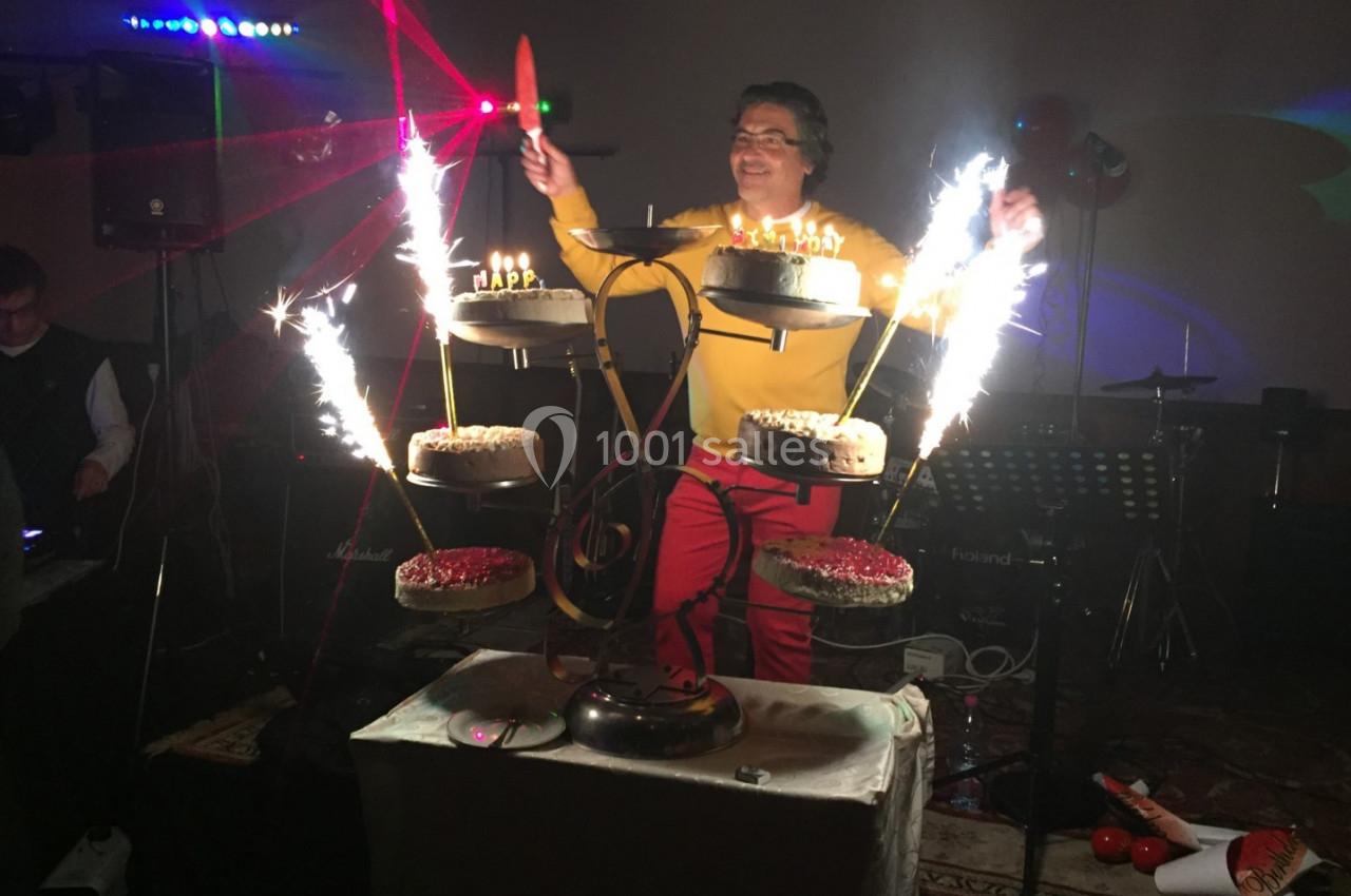 Un homme souriant présente un présentoir à gâteaux illuminé par des cierges magiques dans une ambiance festive.