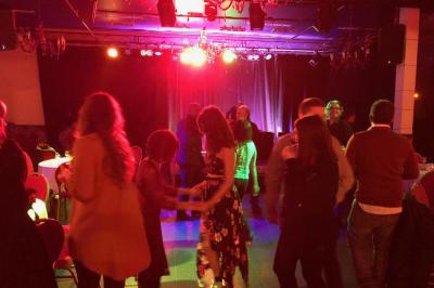 Salle sombre avec un public debout face à une scène éclairée où des musiciens jouent sous des projecteurs colorés.