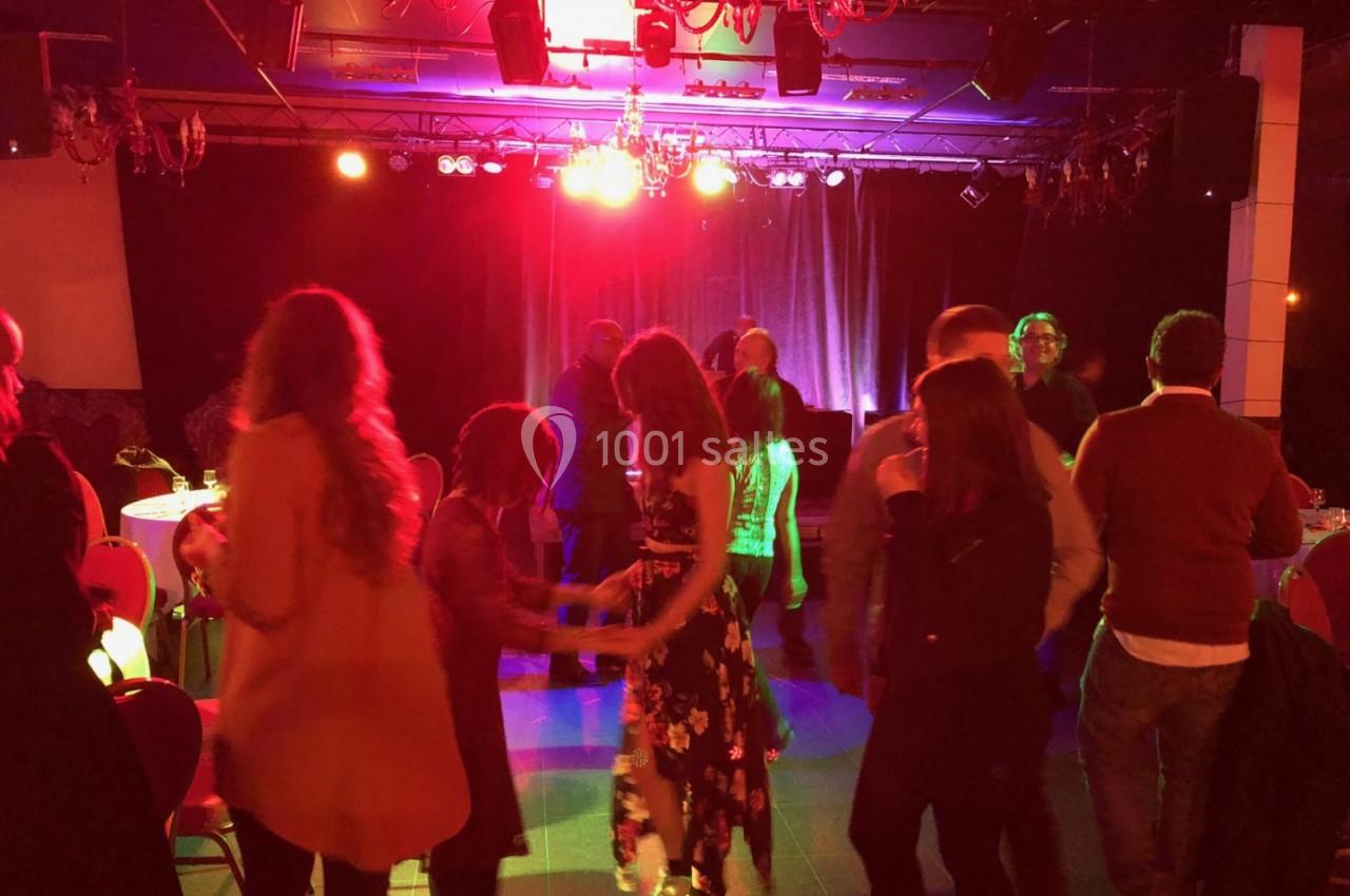 Des personnes dansent dans une salle faiblement éclairée avec des lumières rouges et un rideau de scène en arrière-plan.