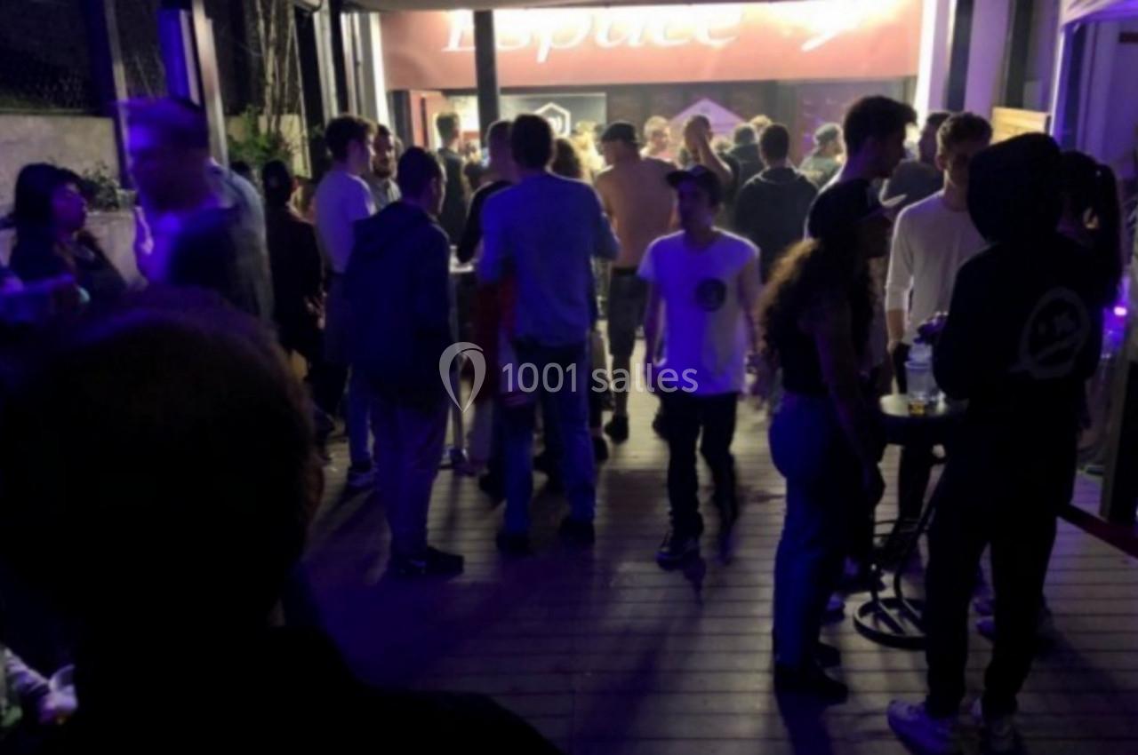 Groupe de personnes discutant et se déplaçant sur une terrasse éclairée par des lumières tamisées en soirée.