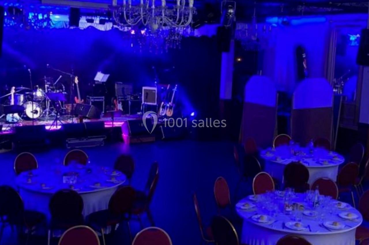 Salle de réception avec tables dressées et une scène équipée d'instruments de musique sous un éclairage bleu.