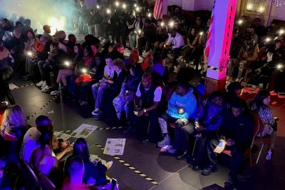 Salle sombre avec un public debout face à une scène éclairée où des musiciens jouent sous des projecteurs colorés.