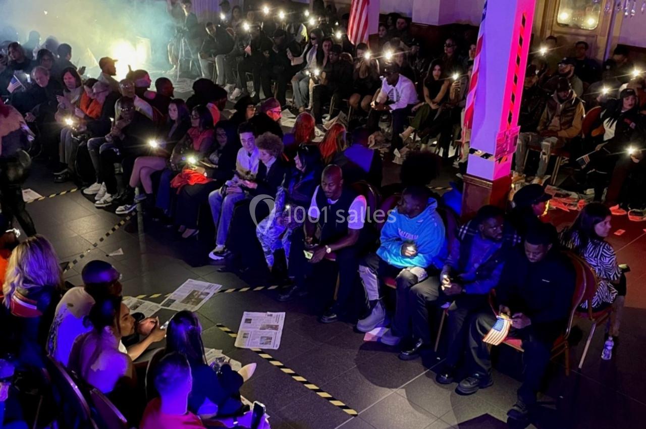 Un groupe de personnes assises dans une salle sombre, éclairées par des lumières de téléphone portable.