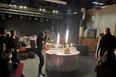 Salle sombre avec un public debout face à une scène éclairée où des musiciens jouent sous des projecteurs colorés.