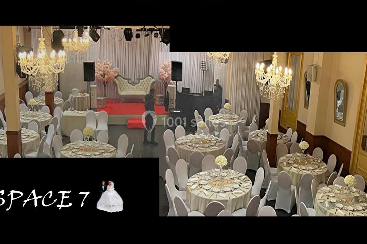 Salle de réception élégante avec tables rondes dressées, chandeliers suspendus et scène décorée en arrière-plan.