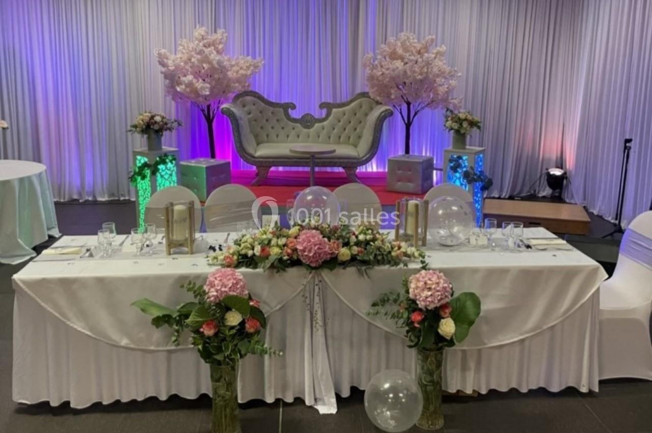 Table décorée avec des fleurs et des ballons devant un canapé élégant, dans une salle ornée de rideaux et éclairages colorés.