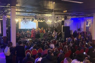 Salle sombre avec un public debout face à une scène éclairée où des musiciens jouent sous des projecteurs colorés.