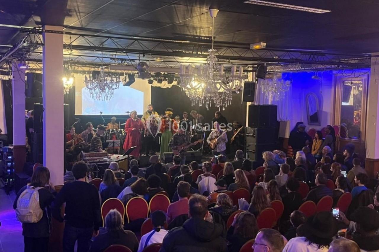 Un groupe de musiciens et chanteurs se produit sur scène devant un public dans une salle éclairée.