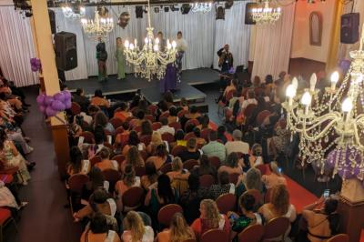 Salle sombre avec un public debout face à une scène éclairée où des musiciens jouent sous des projecteurs colorés.