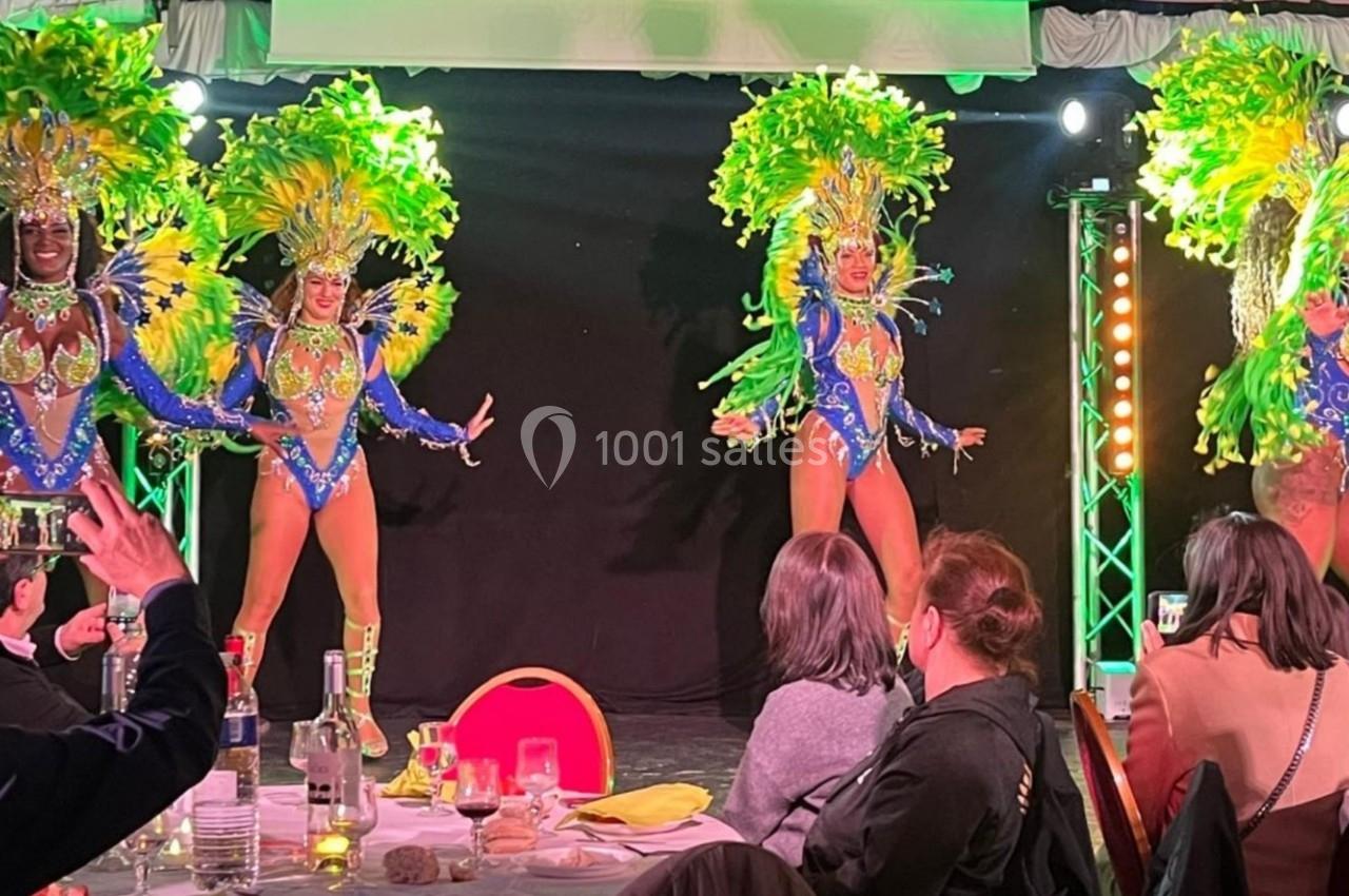 Danseuses en costumes colorés et ornés de plumes se produisant sur scène devant un public assis.
