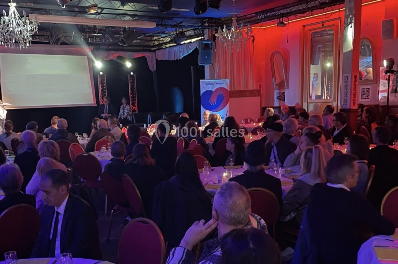 Salle de réception avec des invités assis à des tables rondes, éclairage tamisé et présentation sur scène.