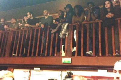 Salle sombre avec un public debout face à une scène éclairée où des musiciens jouent sous des projecteurs colorés.