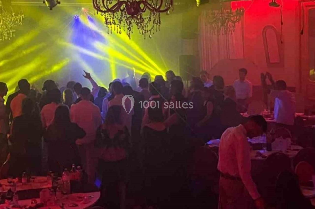 Groupe de personnes dans une salle éclairée par des lumières colorées, avec des tables dressées au premier plan.