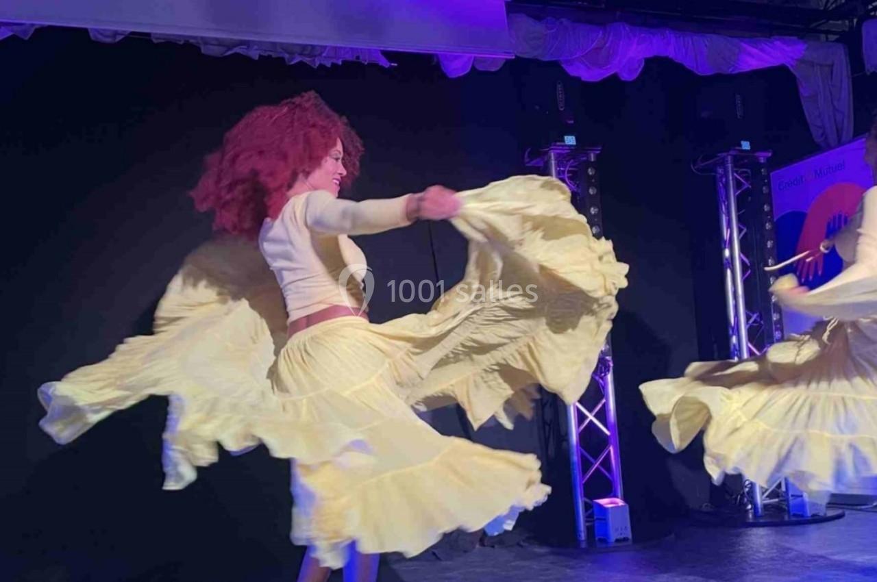 Deux danseuses en jupe jaune virevoltent sur une scène éclairée de lumières violettes.
