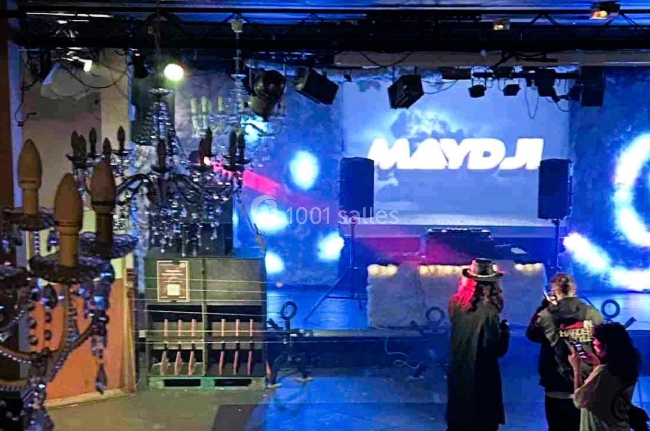 Salle de spectacle avec scène éclairée, projecteurs colorés et trois personnes discutant au premier plan.