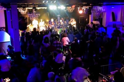 Salle sombre avec un public debout face à une scène éclairée où des musiciens jouent sous des projecteurs colorés.