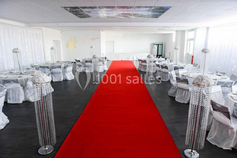 Salle de réception décorée avec des tables nappées de blanc, ornements brillants et tapis rouge central.