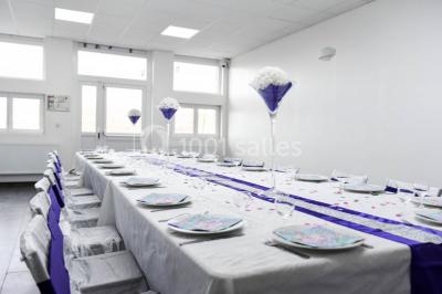 Salle de réception décorée avec des tables rondes dressées, nappes blanches, chandeliers et tapis rouge central.