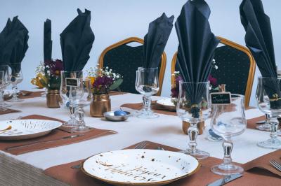 Salle de réception décorée avec des tables rondes dressées, nappes blanches, chandeliers et tapis rouge central.