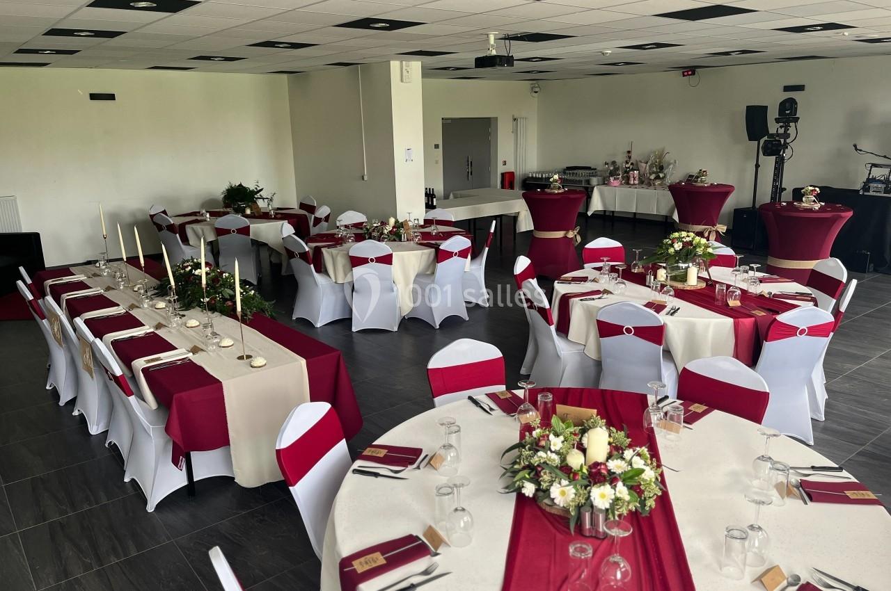 Salle de réception décorée avec des nappes rouges et blanches, tables rondes et rectangulaires ornées de bouquets de fleurs.