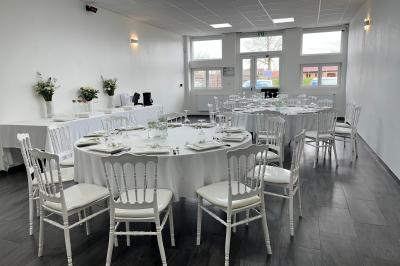 Salle de réception décorée avec des tables rondes dressées, nappes blanches, chandeliers et tapis rouge central.