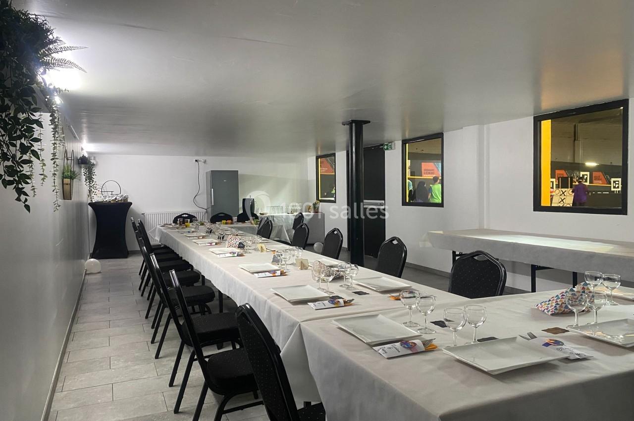 Salle de réception avec tables dressées, nappes blanches, chaises noires et décoration murale végétale.