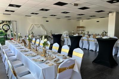 Salle de réception décorée avec des tables rondes dressées, nappes blanches, chandeliers et tapis rouge central.