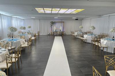 Salle de réception décorée avec des tables rondes dressées, nappes blanches, chandeliers et tapis rouge central.