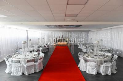 Salle de loisirs avec tables de billard, baby-foot, canapés noirs et murs rouges dans un espace lumineux.