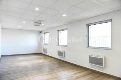 Salle de loisirs avec tables de billard, baby-foot, canapés noirs et murs rouges dans un espace lumineux.