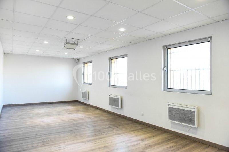 Salle vide avec parquet, murs blancs, plafond à dalles, fenêtres et climatiseurs muraux.