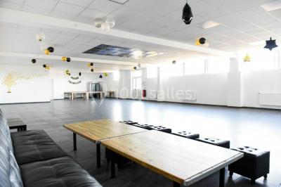 Salle de loisirs avec tables de billard, baby-foot, canapés noirs et murs rouges dans un espace lumineux.