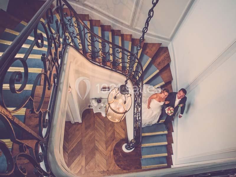 Vue plongeante sur un couple en tenue de mariage montant un escalier en colimaçon dans un intérieur élégant.