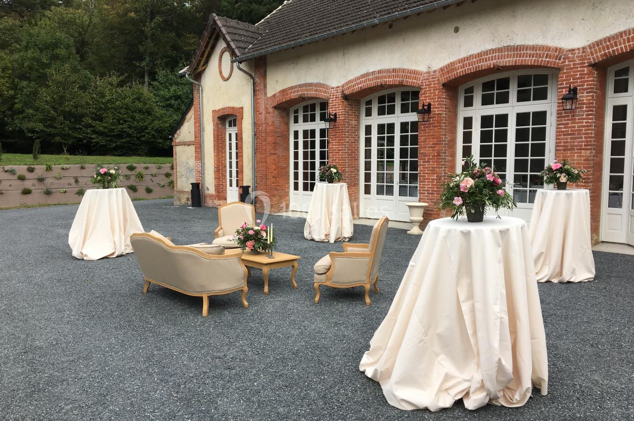 Mobilier élégant et tables drapées installés en extérieur devant une bâtisse en briques avec grandes fenêtres.