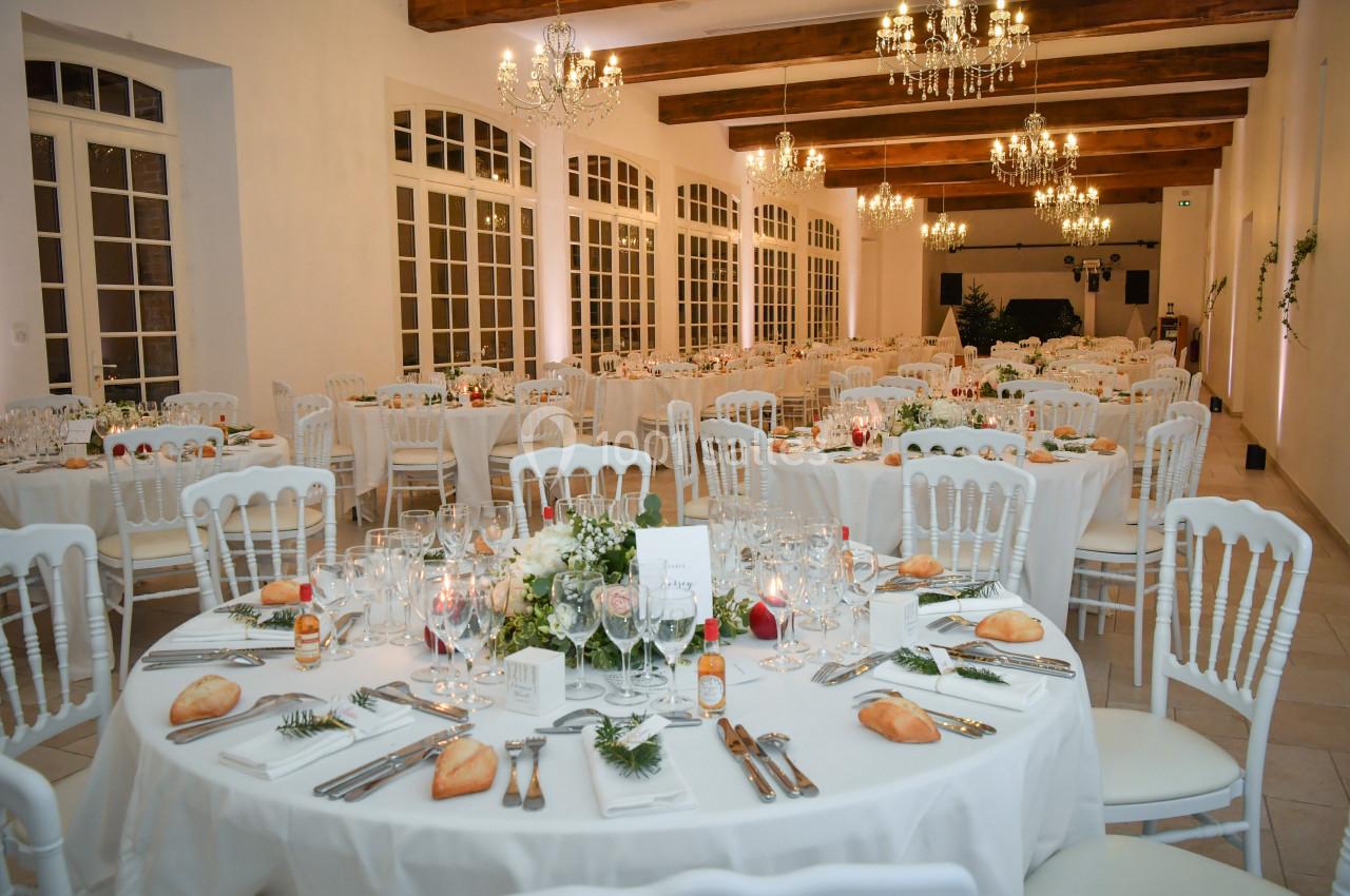 Salle de réception élégante avec tables rondes dressées, décorations florales et chandeliers suspendus.