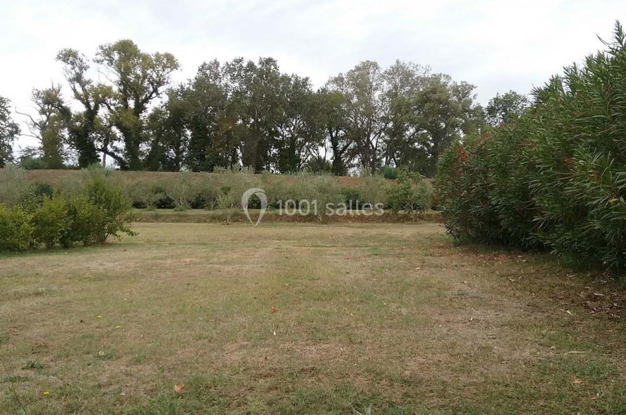 Location salle Fourques (Gard) - Domaine de la Tourette #13 Vue d'un champ herbeux entouré d'arbres et d'arbustes sous un ciel légèrement nuageux.