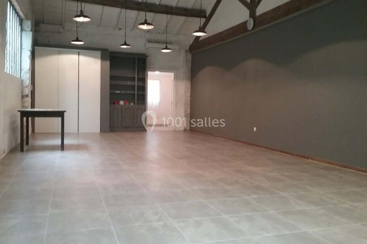 Location salle Fourques (Gard) - Domaine de la Tourette #6 Salle vide avec sol en carrelage, murs gris et blancs, poutres apparentes au plafond, éclairée par des suspensions.