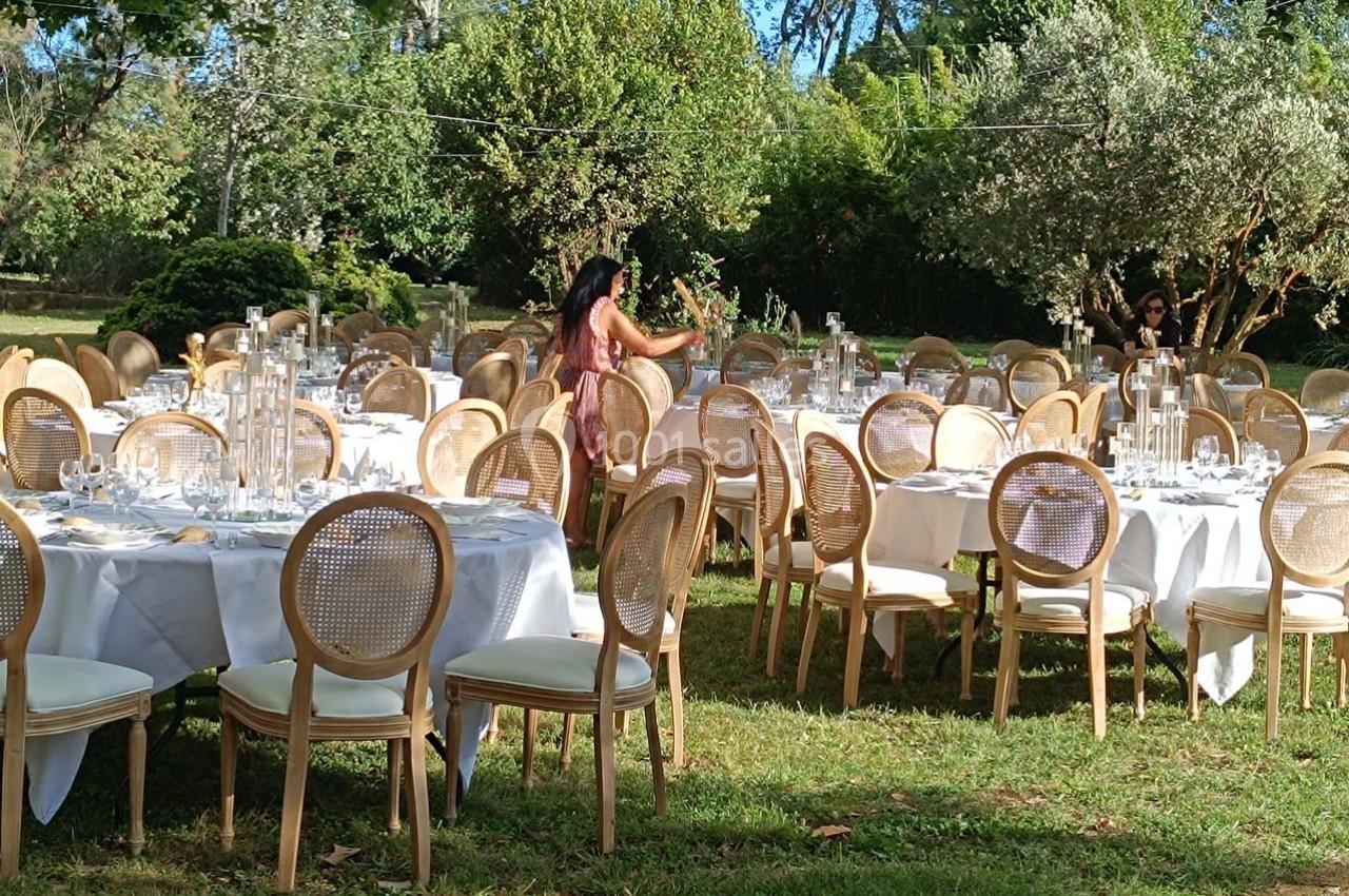 Location salle Fourques (Gard) - Domaine de la Tourette #3 Tables rondes dressées avec nappes blanches et chaises en bois dans un jardin, préparées pour un événement en plein air.