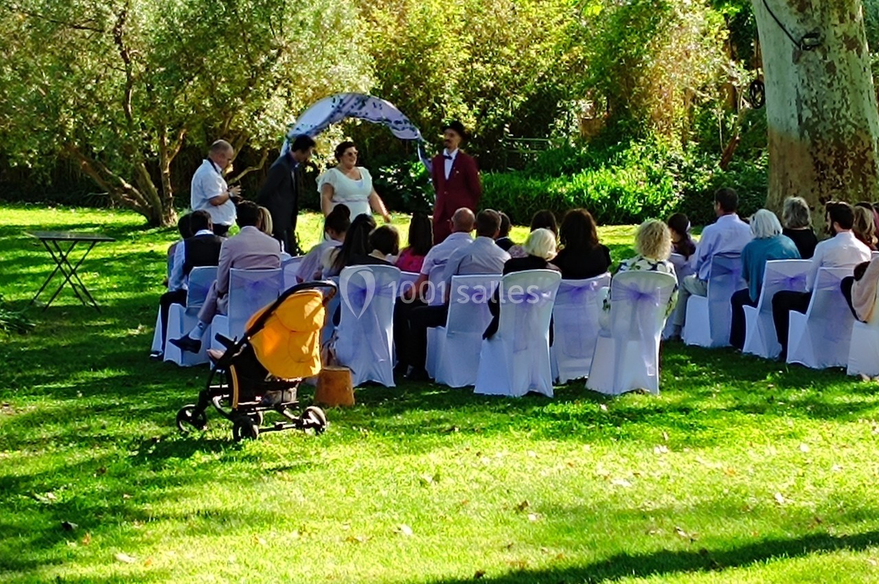 Cérémonie de mariage en plein air avec des invités assis sur des chaises blanches, sous des arbres verdoyants.