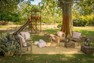 Arbre feuillu dans un jardin ensoleillé avec une structure de jeu pour enfants incluant un toboggan.