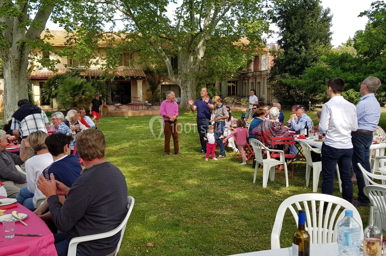 Groupe de personnes réunies dans un jardin, assises ou debout autour de tables, lors d'un repas en plein air.