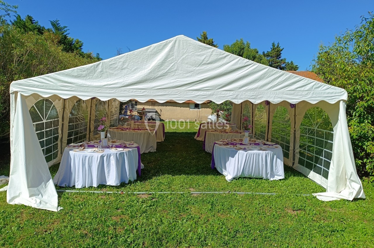Tente blanche installée dans un jardin, abritant des tables rondes décorées pour un événement.