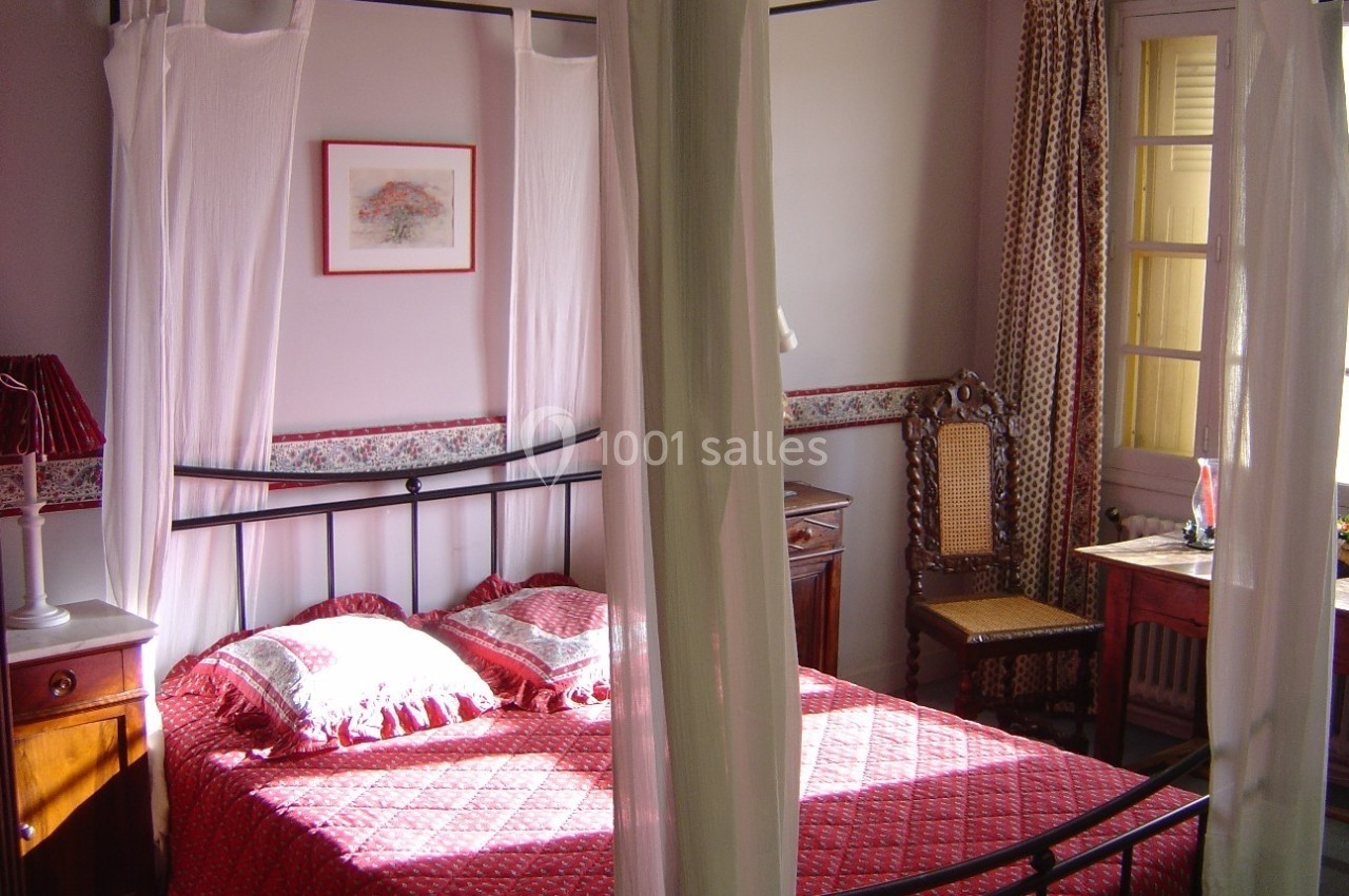 Lit à baldaquin avec drapés blancs dans une chambre lumineuse, décorée de meubles en bois et d'un tableau au mur.