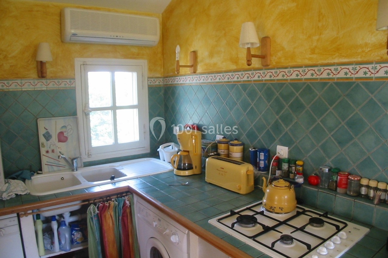 Cuisine équipée avec carrelage vert, appareils électroménagers jaunes, évier, fenêtre et étagères avec condiments.